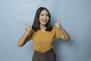 Young pretty woman smiling joyfully and looking happy, feeling carefree and positive with both thumbs up isolated by blue background photo