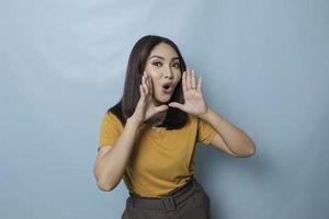 Surprised Asian woman reclines on her hands and shouting while looking at the camera over blue background photo