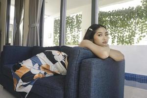 Young Asian woman sitting on the couch in the living room looks sorrowful. photo