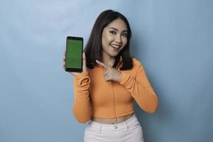 An excited young woman pointing at copy space on her smartphone in her hand, isolated on blue background photo