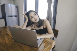 la joven asiática pasa su tiempo en casa sentada en el comedor frustrada y cansada trabajando en su computadora portátil. foto