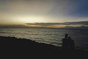 shilloutte de una pareja romántica saliendo en una playa durante una puesta de sol foto