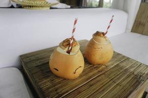 two coconut juices with paper straws placed on a wooden table photo