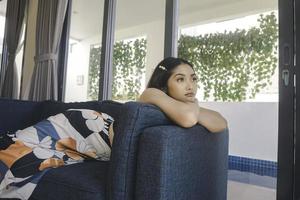 Young Asian woman sitting on the couch in the living room looks sorrowful. photo