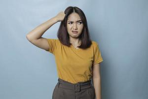 una joven asiática insatisfecha mira la cámara posando en un fondo azul, una chica descontenta con una camiseta amarilla, las expresiones faciales irritadas muestran una imagen conceptual de actitud negativa foto