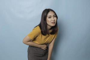 Young Asian woman with arms on stomach and bending over with stomachache expression photo