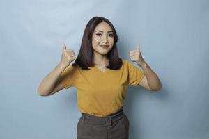 Young pretty woman smiling joyfully and looking happy, feeling carefree and positive with both thumbs up isolated by blue background photo