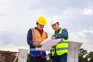 ingeniero y trabajador de capataz revisando el proyecto en el sitio de construcción, ingeniero y constructores en cascos discutiendo planos en el sitio de construcción, conceptos de trabajo en equipo foto