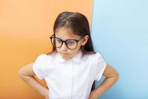 A 7-year-old girl with glasses with an angry face and hands on her sides. Children's education, learning concept photo