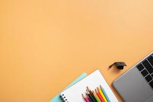 Stationary and laptop with graduated cap on colored background. Copy space. Children work space top view, flat lay. Online learning concept photo