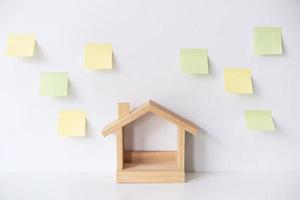 Wooden model house with empty sticky notes on white wall with copy space photo