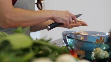 Woman closeup seeing only hands using small knife cutting mushrooms into the bowl video