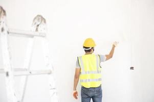 A view of the painter behind the wall painter with a paint roller and split bucket on a large empty space with a wooden staircase. photo