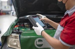 mecánico profesional y control del motor del automóvil con software de diagnóstico por computadora. Mecánico experto que trabaja en un taller de reparación de automóviles. foto