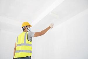 A view of the painter behind the wall painter with a paint roller and split bucket on a large empty space with a wooden staircase. photo