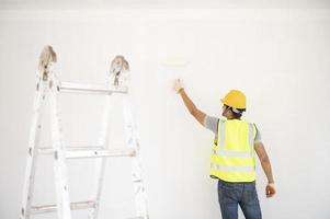 A view of the painter behind the wall painter with a paint roller and split bucket on a large empty space with a wooden staircase. photo