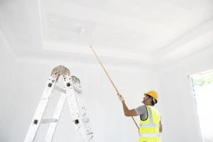 A view of the painter behind the wall painter with a paint roller and split bucket on a large empty space with a wooden staircase. photo