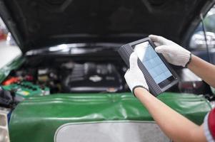 mecánico profesional y control del motor del automóvil con software de diagnóstico por computadora. Mecánico experto que trabaja en un taller de reparación de automóviles. foto