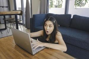 Young Asian woman spend her time at home sitting in the living room shocked while working on her laptop. photo