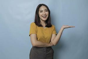 An excited young woman presenting and pointing copy space on her side, isolated on blue background photo