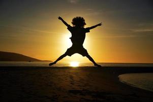 SILHOUETTE OF AN AFRO HAIRED MAN JUMPING WITH A SUNSET BACKGROUND photo