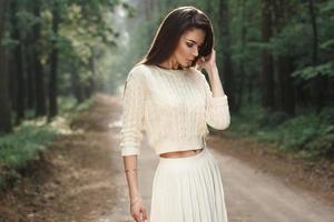 Portrait of a pretty woman in a white sweater on the road in the forest with fog. photo