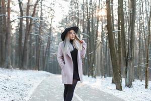 Young beautiful girl in a stylish hat and coat walking in the winter park photo