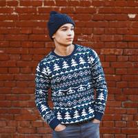 Man in a knitted warm sweater with Christmas patterns and hat standing near red brick wall photo