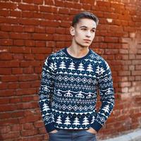 Young handsome man in a knit sweater with Christmas ornaments on a background of red brick wall photo