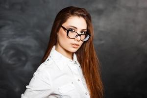 Young beautiful girl in stylish glasses and a white blouse fashion on a dark background in the studio. Office Style photo