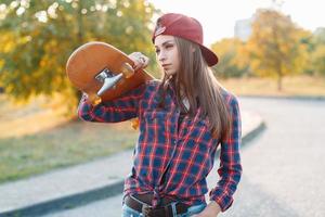 Young beautiful woman holding a skateboard in the park at sunset photo