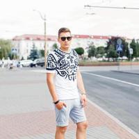 apuesto joven en camiseta y pantalones cortos posando en el fondo de la ciudad. foto