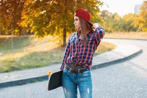 joven elegante con patineta parada en el parque en un día soleado foto