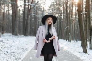 Stylish young girl walking in a winter sunny day on the background of the park with snow photo