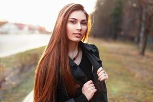 Beautiful stylish girl in a black cloak walking in the park in the spring day at sunset. photo