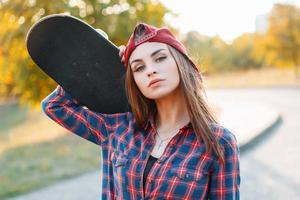 Closeup portrait of a young girl in a cap holding a skateboard in the park at sunset. photo