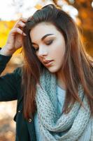 Close-up portrait of a young beautiful girl in knitted sweater, scarf and a black jacket in the autumn park photo