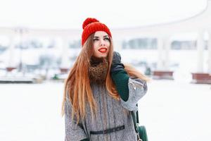 Young cute girl with a beautiful smile in a red knitted hat and coat on a winter day photo
