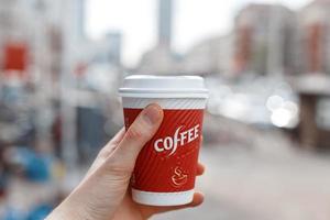 Hand holding a red cup of coffee on the background of the city. photo