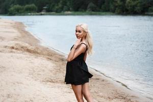 hermosa mujer hermosas piernas femeninas entran en el agua en vestido negro en la playa foto