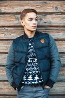 Handsome young man in a knitted sweater and winter warm jacket near the vintage wooden wall. photo