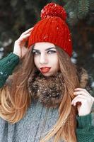 Pretty girl with beautiful blue eyes in a red hat and coat standing near spruce photo