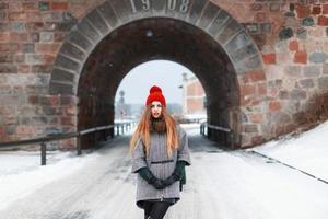 una joven hermosa vestida de invierno se encuentra en el fondo de un arco de piedra foto