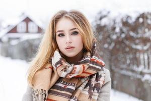 Close-up portrait of a young beautiful girl with winter vintage scarf on the background of the village photo