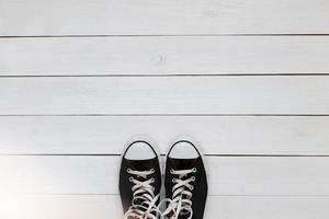 Black sneakers with laces on a white wooden floor. top view photo