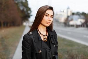 Young fashionable girl in spring black jacket on a background of city buildings photo