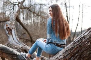 una joven hermosa con chaqueta vaquera y jeans se sienta en un árbol y sueña. foto