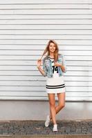 Cheerful beautiful woman with a smile in a denim jacket standing near a white wooden wall. photo