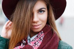 Close-up portrait of a beautiful young girl in a burgundy hat and stylish scarf photo