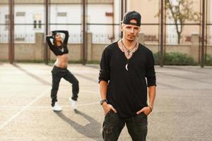 retrato de un hombre guapo de hip hop con ropa negra elegante. en el fondo una hermosa niña bailando foto